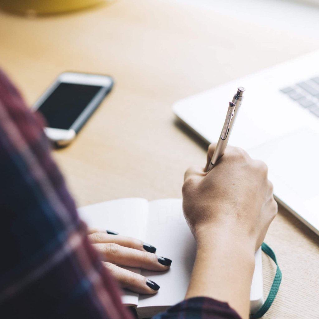 Writing in a notebook, next to a computer