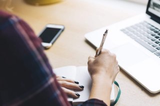Writing in a notebook, next to a computer