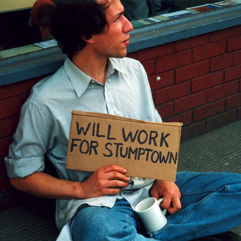 Raymond holding a signs that says "WILL WORK FOR STUMPTOWN" - part of an early art project.