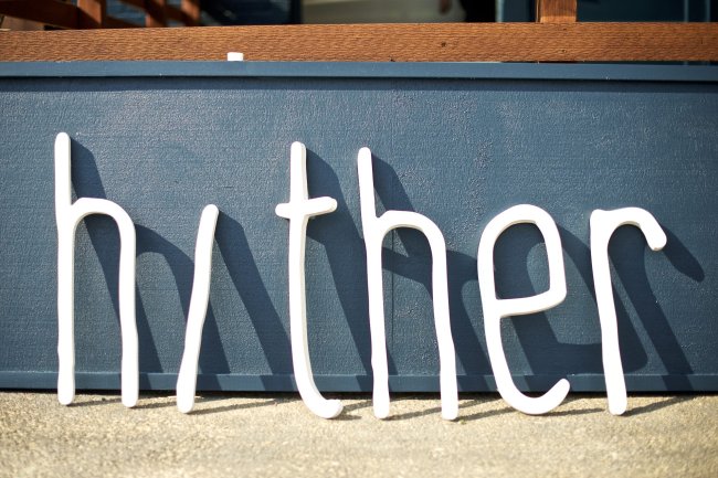 All the letters from the Hither Coffee + Goods sign leaning against a wall