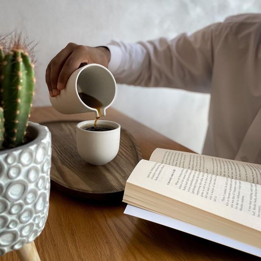 Person pouring coffee and reading a book at Stanza