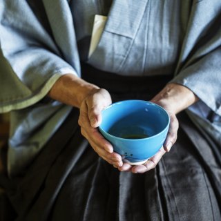 Man holding blue tea bowl during tea ceremony.